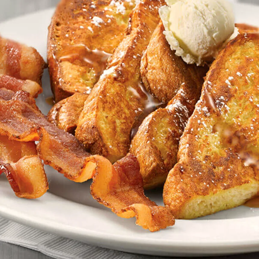 Thick slices of French toast dusted with sugar, with strips of bacon and a scoop of ice cream