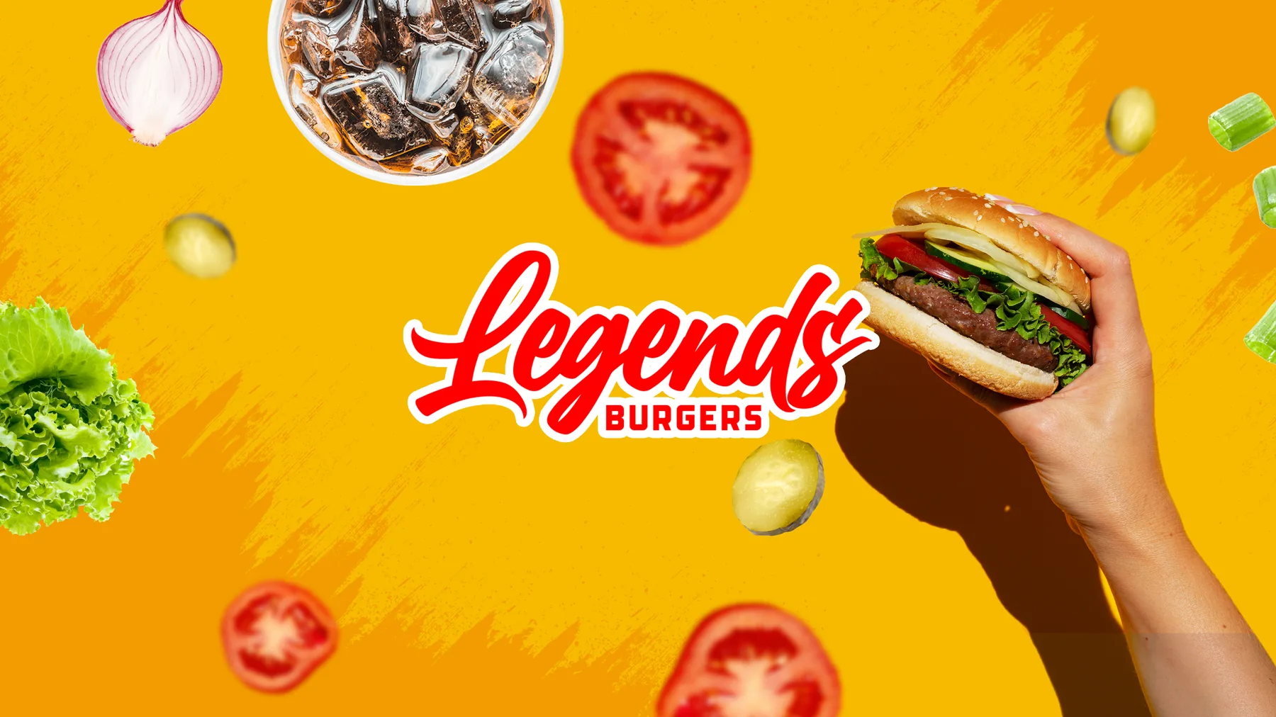 A hand holding a Legends burger against a yellow background scattered with
              lettuce, tomato, onion and a fountain drink, beside the Legends Burgers logo