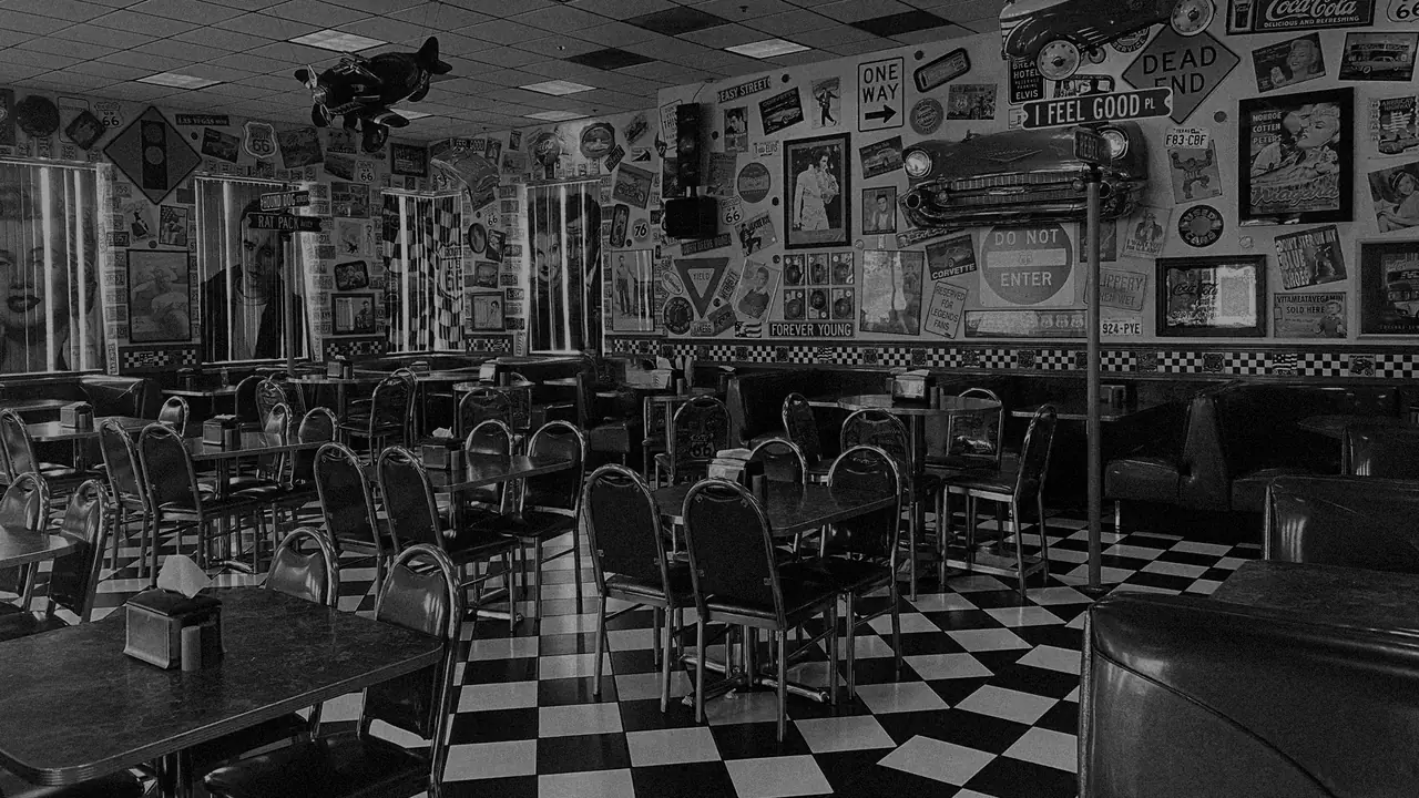 The Legends dining room: vinyl booths and chairs on a black-and-white
                    checkerboard floor, under a wall of framed photographs and road signs
